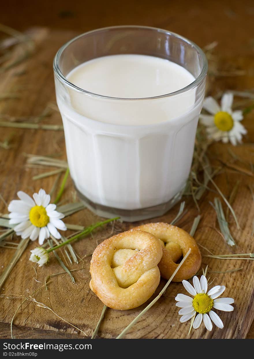 Glass of milk on a board with two pretzels and chamomile