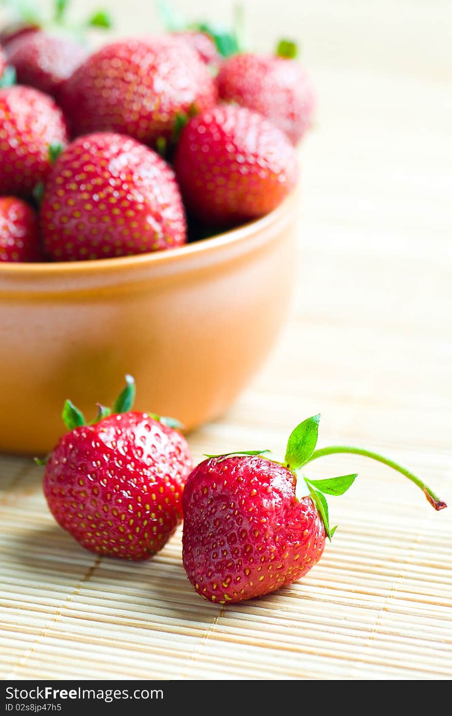 Ripe strawberries in ceramic bowl on wooden background