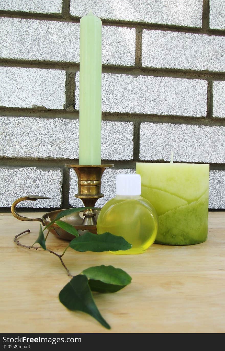 Green long candle in a golden candle holder, big green candle, soap bottle and leafs on a wooden table. Green long candle in a golden candle holder, big green candle, soap bottle and leafs on a wooden table.