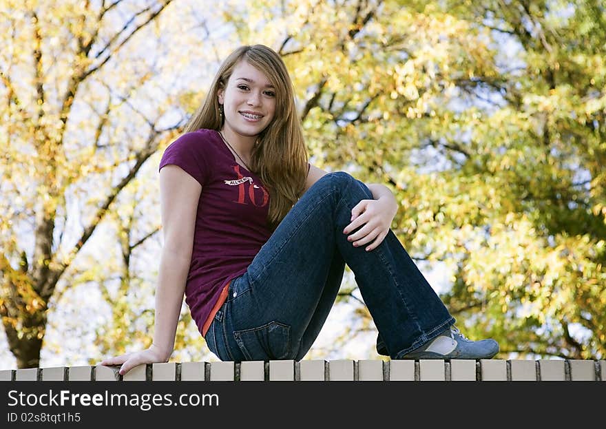 Teenage girl sitting on a white brick wall in early Fall. Teenage girl sitting on a white brick wall in early Fall