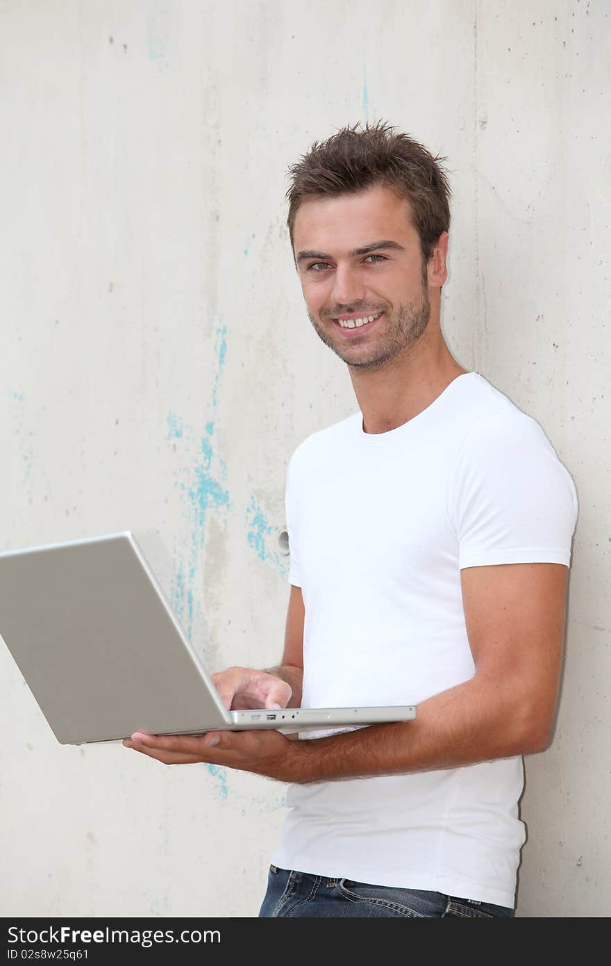 Young man standing against a wall with laptop computer. Young man standing against a wall with laptop computer