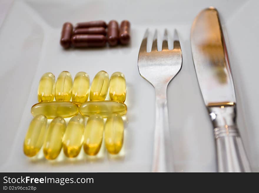 Capsules of lecithin and iron on the white plate with the fork and knife. Capsules of lecithin and iron on the white plate with the fork and knife