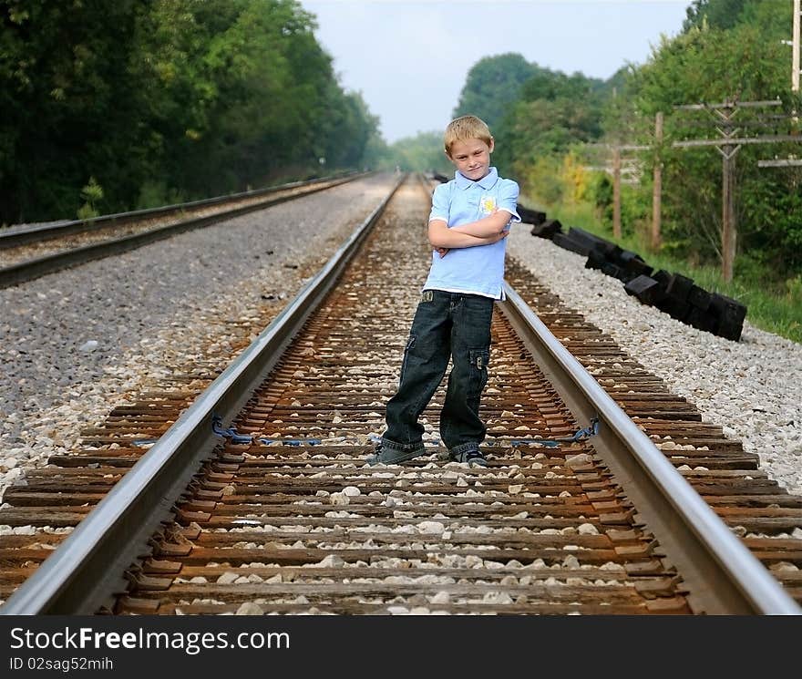 A cute young boy stands on railroad tracks to pose for a photograph.