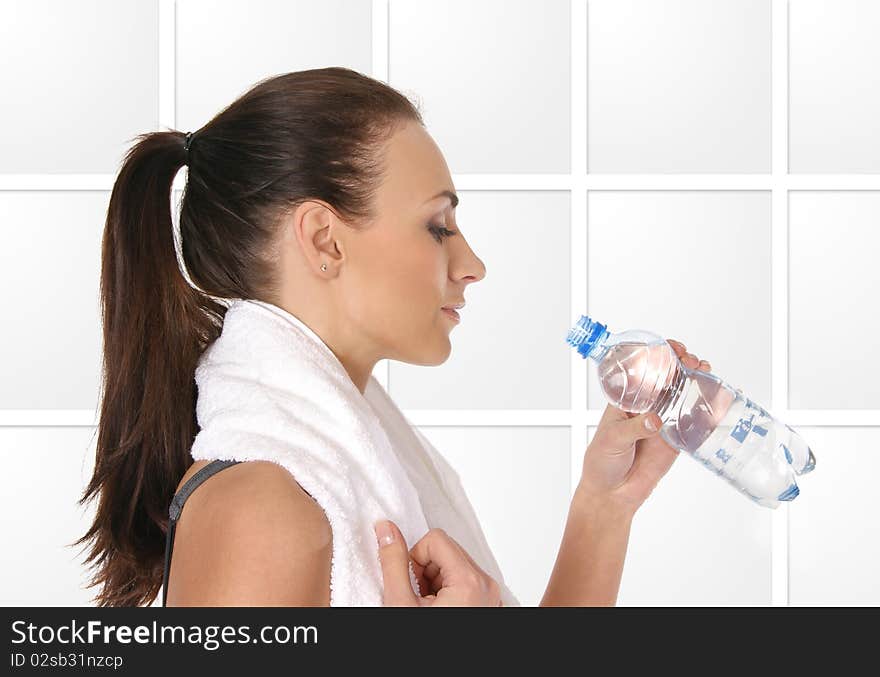 A young and sporty female is drinking water after training. The image is taken on a light gray abstrack background.