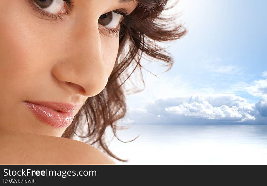 Portrait of a young and attractive brunette girl. The image is taken outdoors, on a sky and water background.