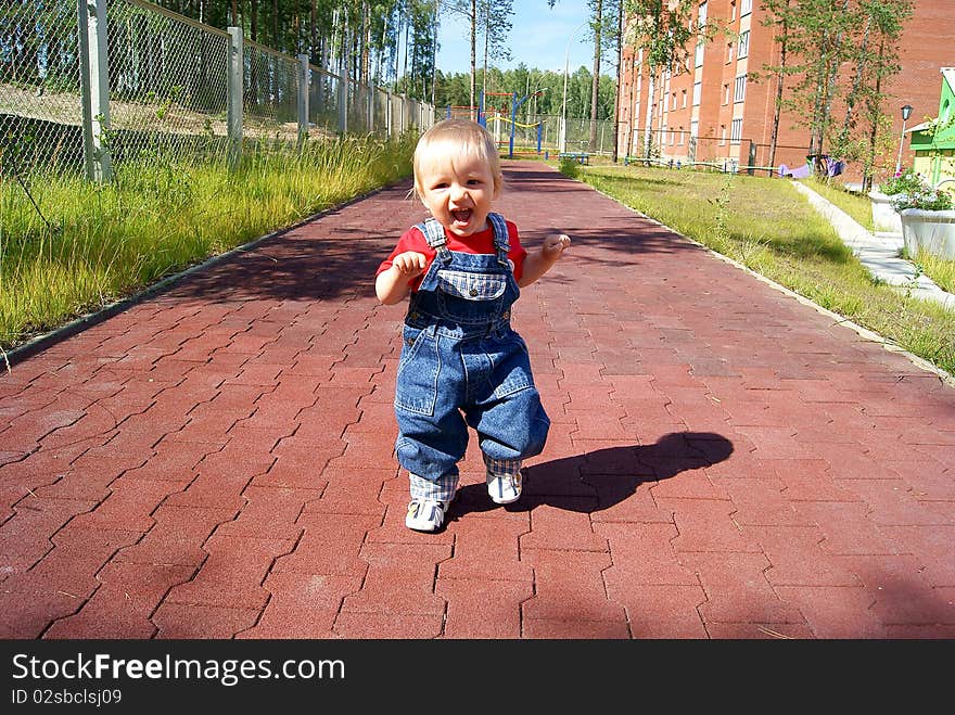 In the summer on a children's athletic field the small smiling child runs on a path. In the summer on a children's athletic field the small smiling child runs on a path