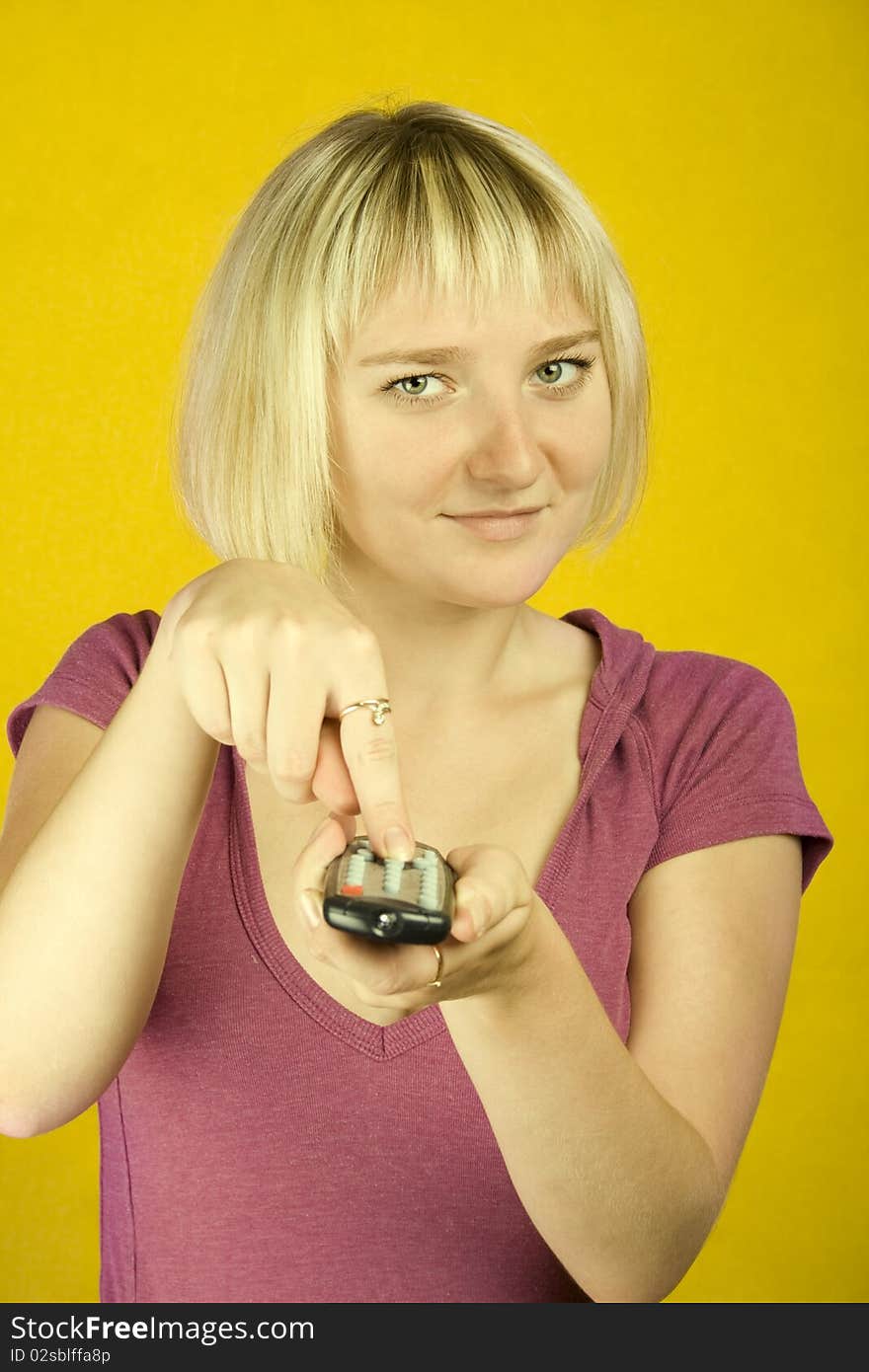 Young woman on yellow background holding a remote control designed into the frame. Finger on the other hand presses the button. Young woman on yellow background holding a remote control designed into the frame. Finger on the other hand presses the button.