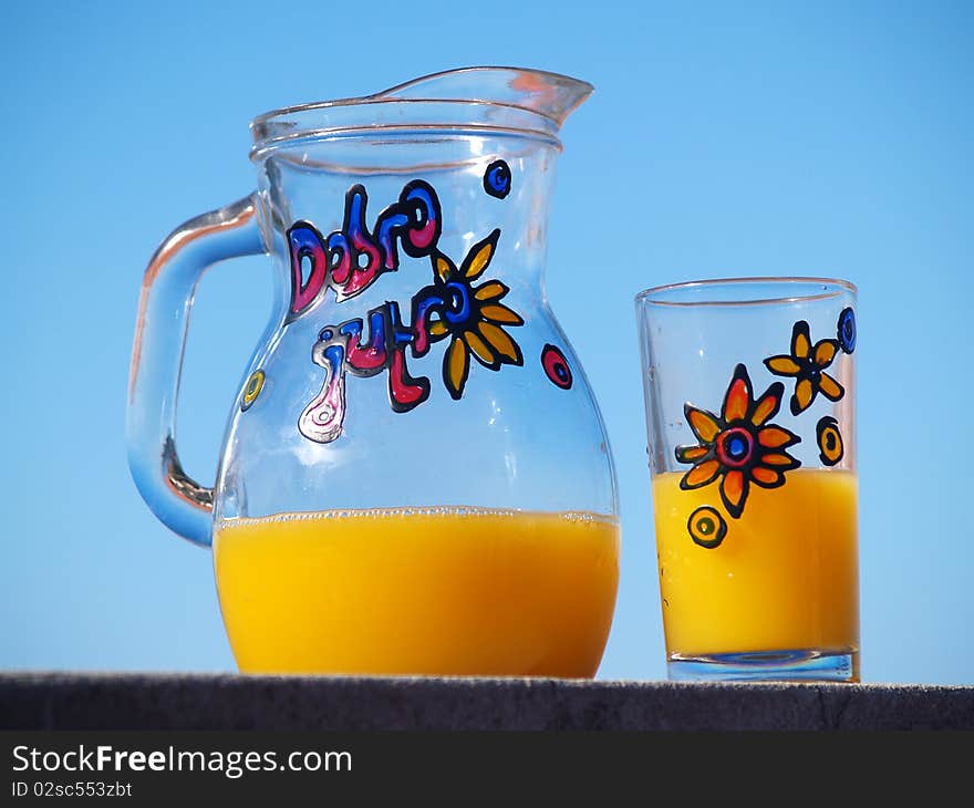 Jar and glass with orange juice, blue sky at the background. Jar and glass with orange juice, blue sky at the background