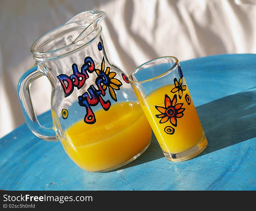 Glass and jar filled with orange juice standing at the blue table. Glass and jar filled with orange juice standing at the blue table