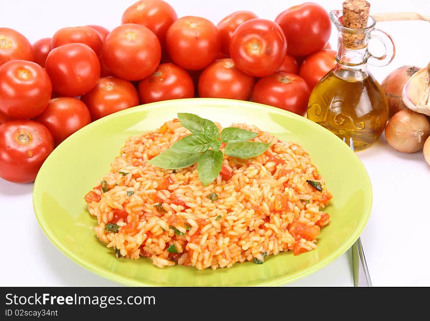 Risotto with tomatoes on a green plate decorated with basil with fresh tomatoes, onions, garlic and olive oil on white background