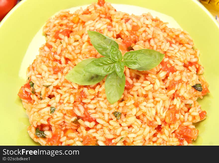 Risotto with tomatoes on a green plate decorated with basil in close up