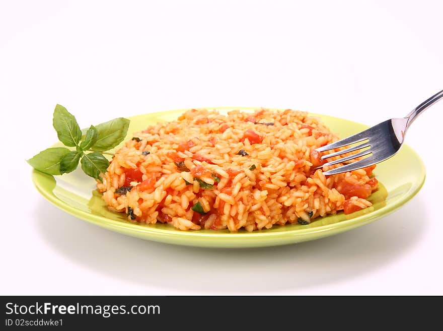 Risotto with tomatoes on a green plate decorated with basil being eaten with a fork