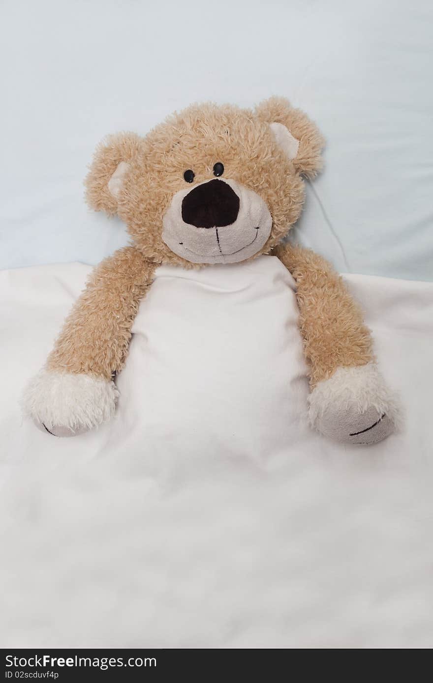 An adorable teddy bear laying in bed, under the sheets.