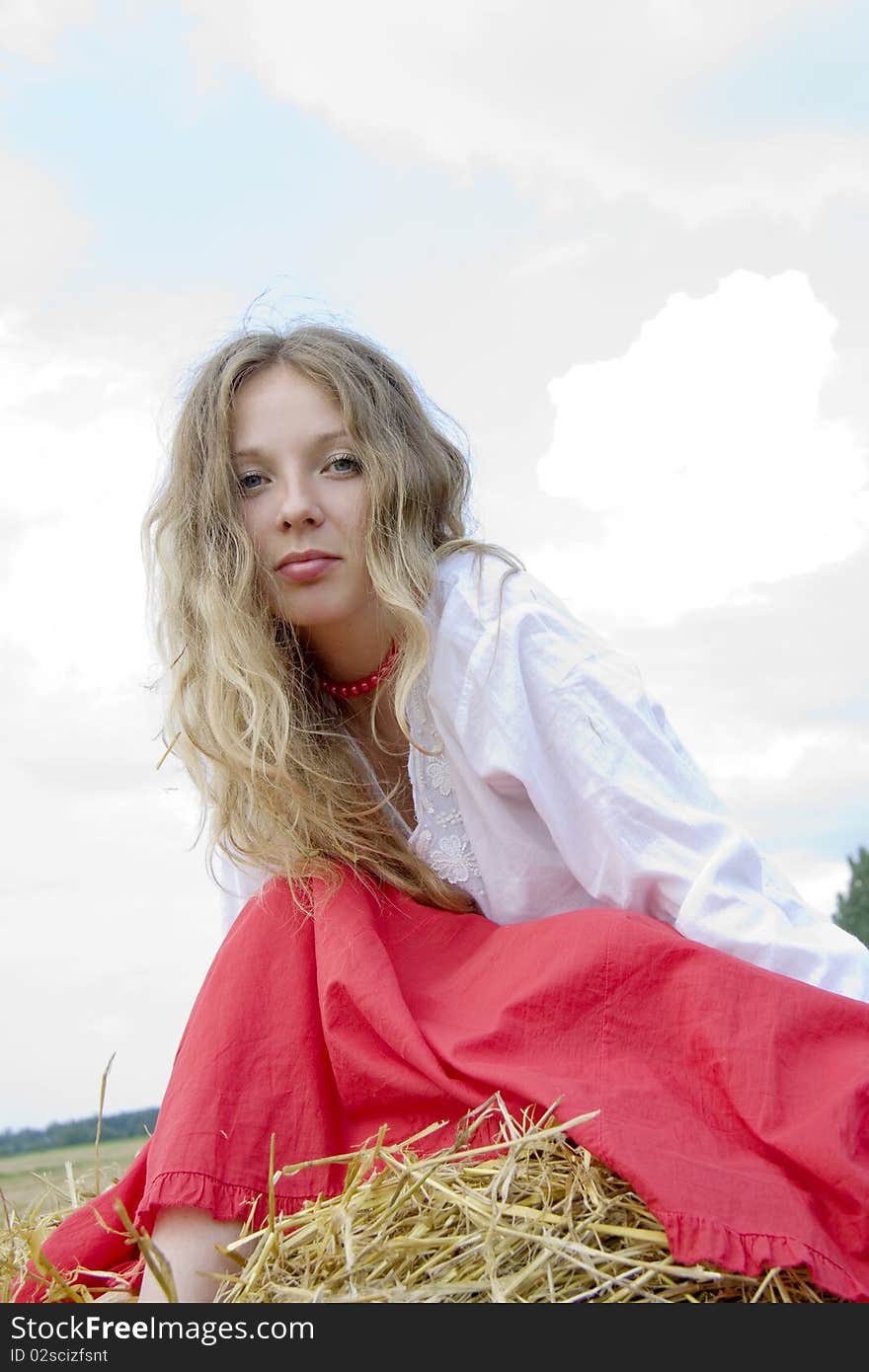 Woman with long hair in red clothes sits in the summer on straw. Woman with long hair in red clothes sits in the summer on straw