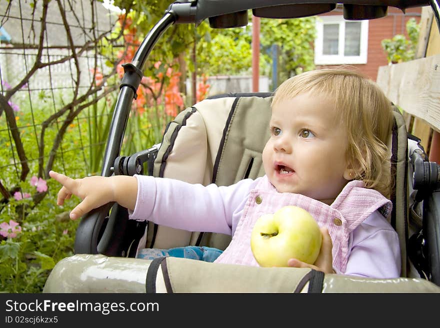 The small child sits in a children's carriage and a hand shows aside. The small child sits in a children's carriage and a hand shows aside