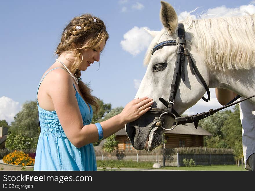 The woman in a blue dress costs and irons a white horse. The woman in a blue dress costs and irons a white horse