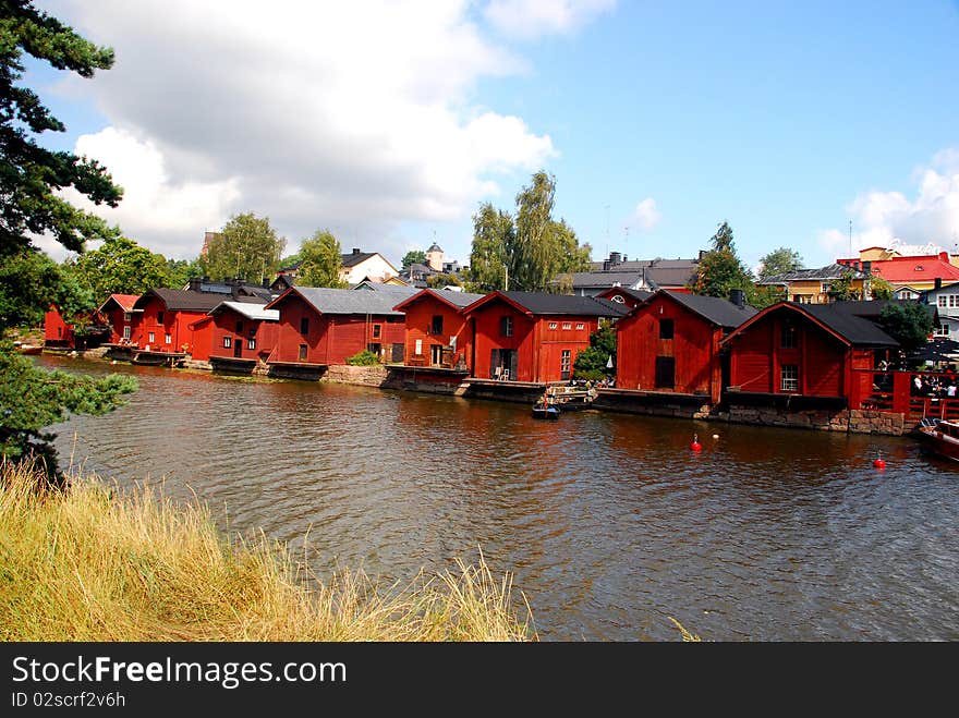 A tipical landscape in Finland in the city of Porvoo, with red houses rounded by trees and t heblue and cloudy sky in the background.