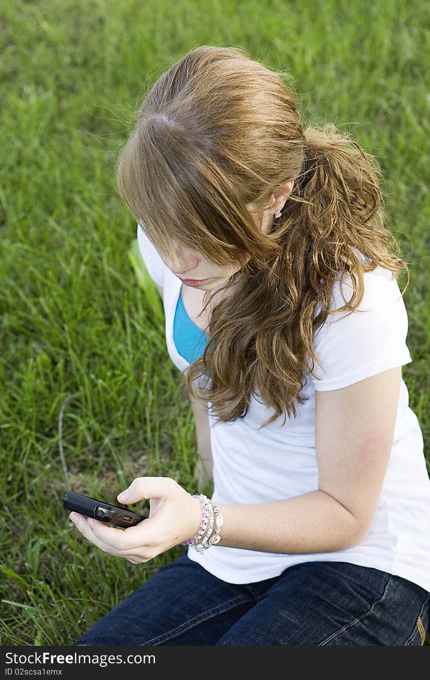 Teenage girl sitting in grass checking her cell phone. Teenage girl sitting in grass checking her cell phone