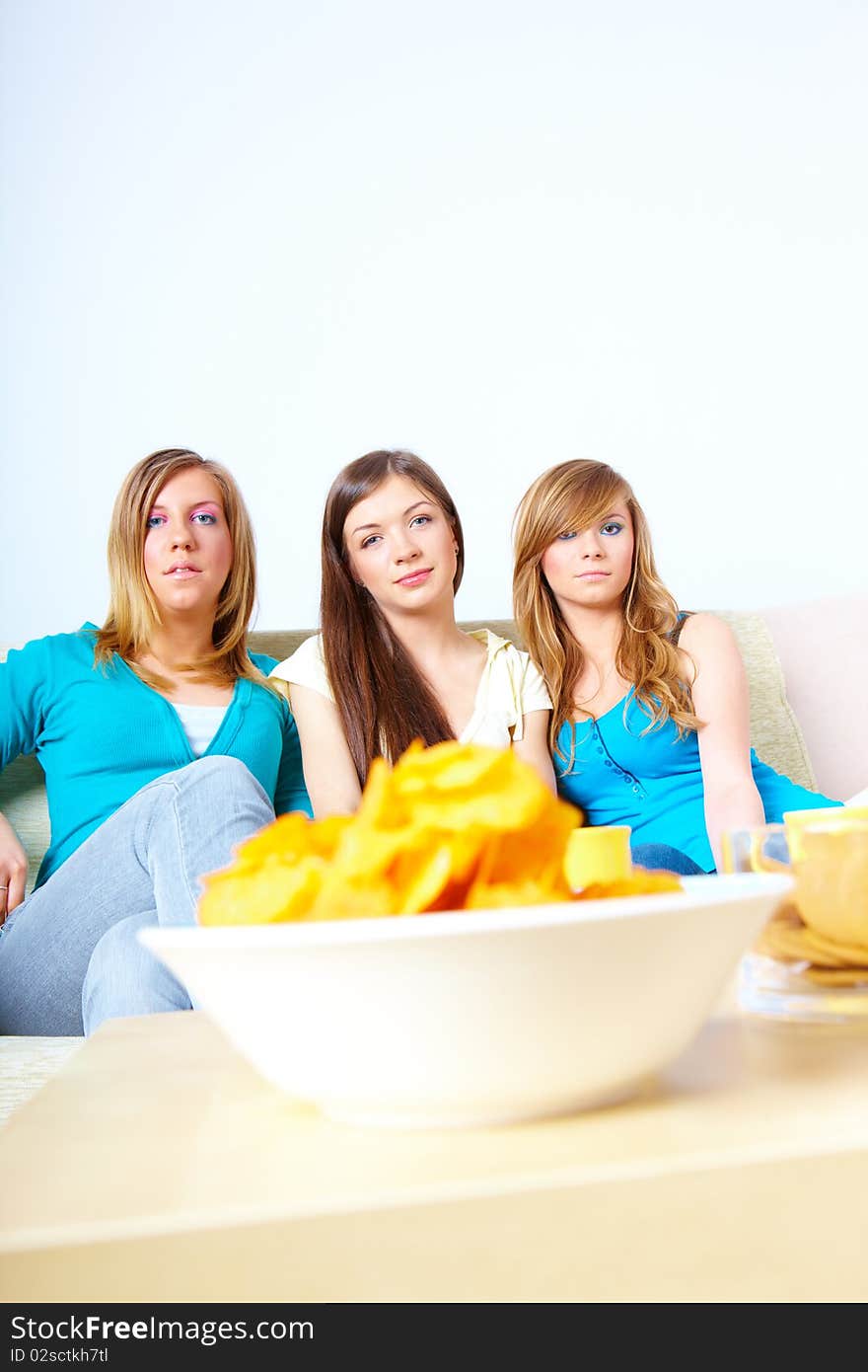 Three happy friends beautiful girls sitting on sofa in home with chips. Three happy friends beautiful girls sitting on sofa in home with chips