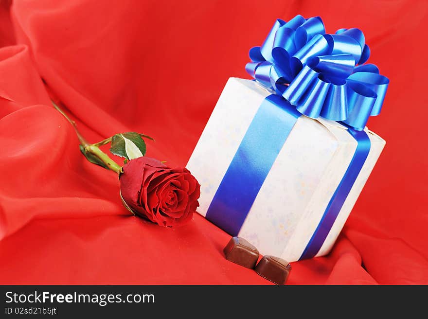 Beautiful red rose, gift and chocolate on red close up