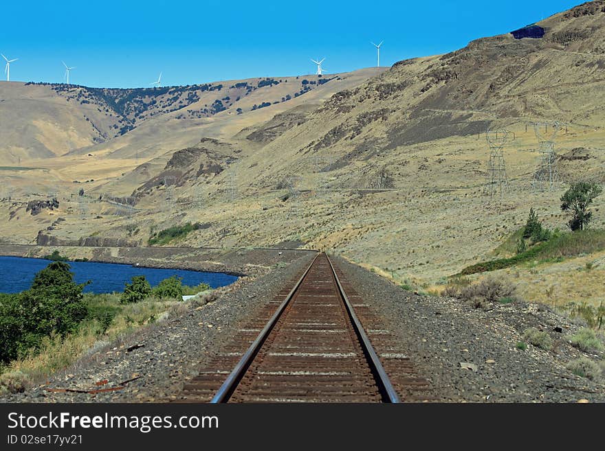 Train tracks in Oregon, next To the Columbia River with wind mills and Electric towers as a background. Train tracks in Oregon, next To the Columbia River with wind mills and Electric towers as a background