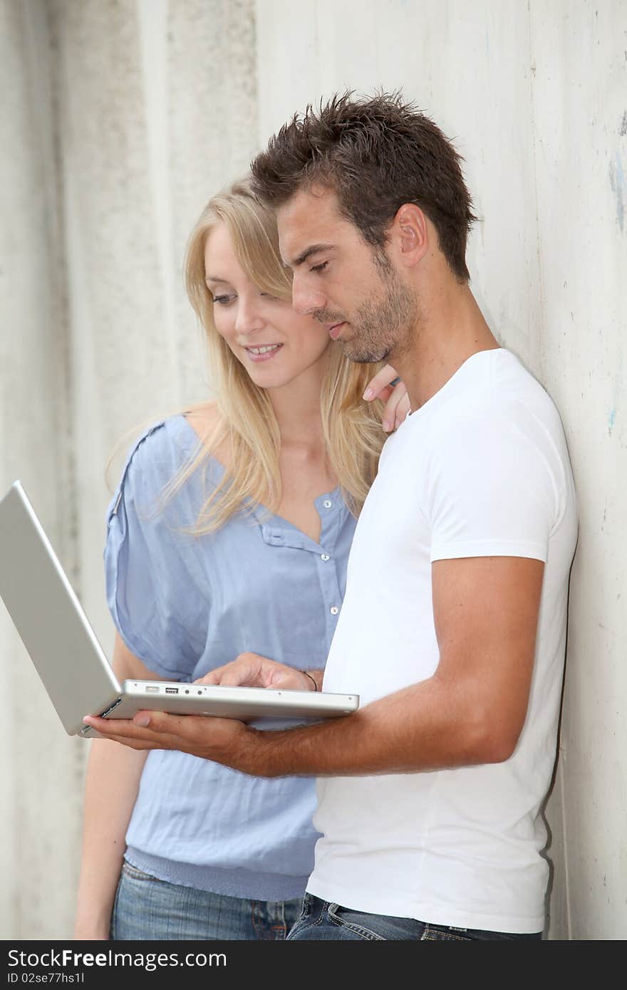 Couple standing against a wall with laptop computer. Couple standing against a wall with laptop computer