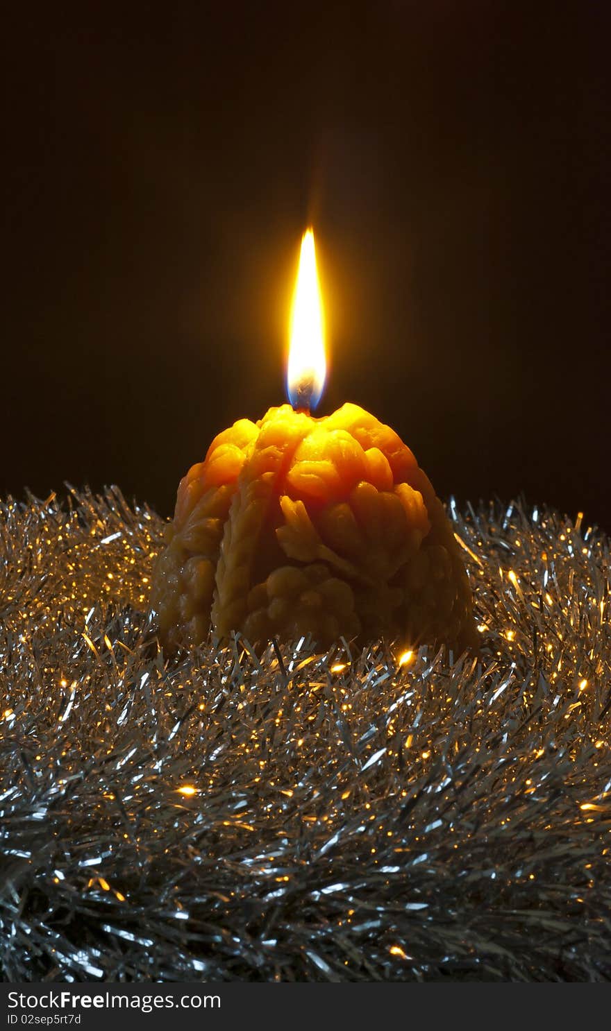 Christmas candle with flame nestled in a bed of silver tinsel on a black background. Christmas candle with flame nestled in a bed of silver tinsel on a black background