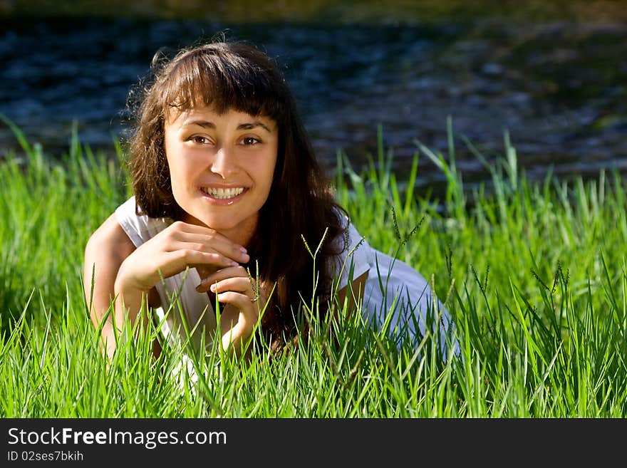 Beautiful young girl liying on green grass near the blue stream. Beautiful young girl liying on green grass near the blue stream