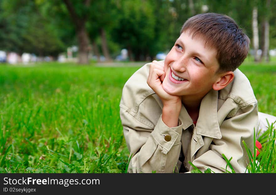 Young beautiful happy boy lays on a grass