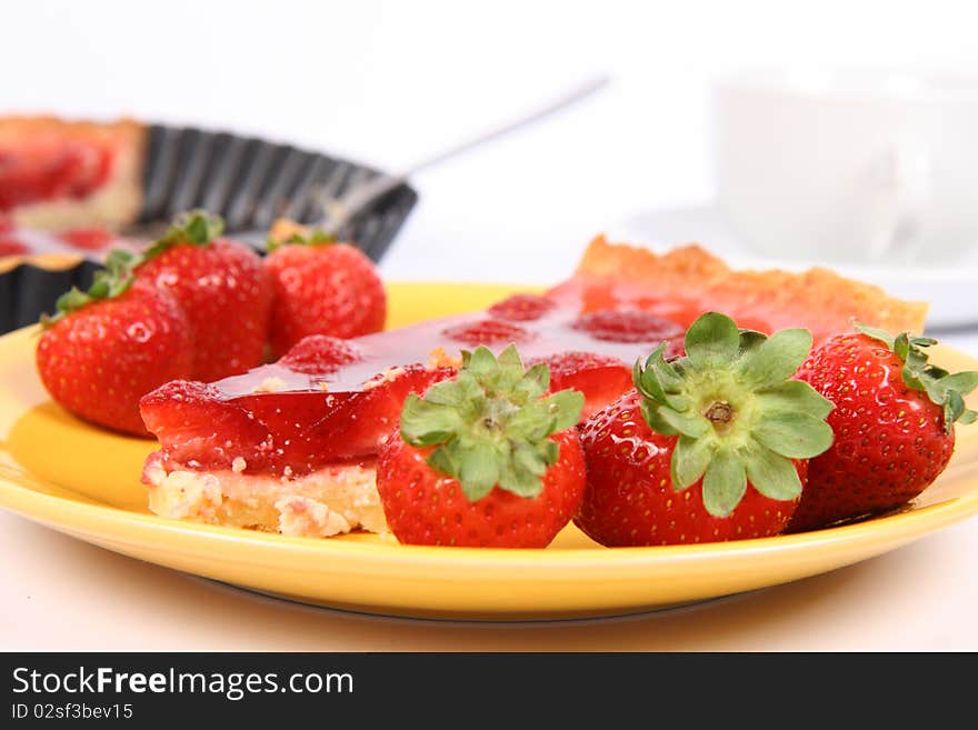 Piece of Strawberry Tart on a yellow plate decorated with strawberries with a cup of coffee and a tart pan in the background