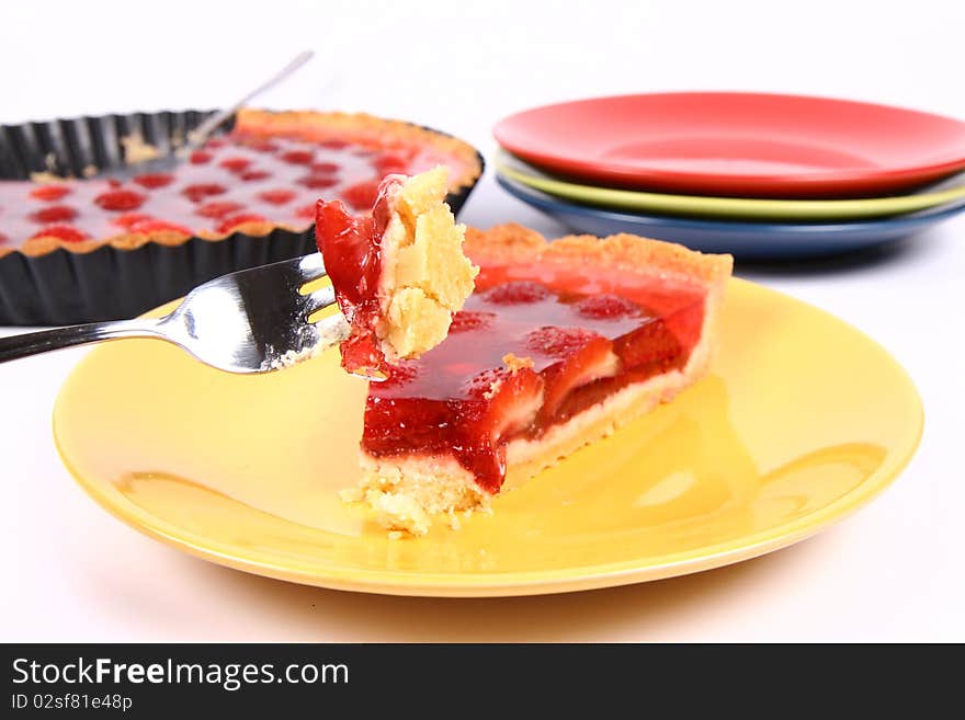 Piece of Strawberry Tart on a yellow plate a tart panand plates in the background and some of the tart on a fork