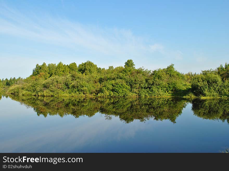 Green trees and sky reverberate in blue river. Green trees and sky reverberate in blue river