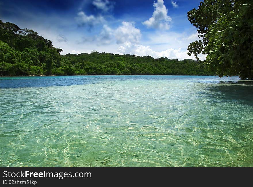 View of clear tropical waters with blue sky and lush green shoreline. View of clear tropical waters with blue sky and lush green shoreline