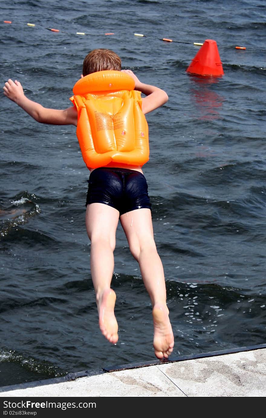 The child in a life jacket jumps in a reservoir.