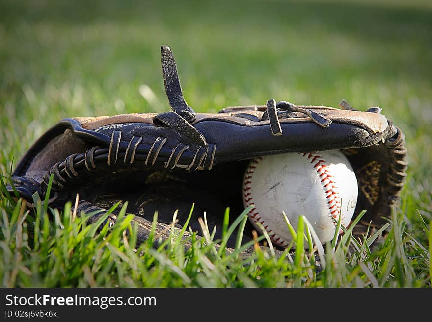 A baseball and glove laying in the grass on a field. A baseball and glove laying in the grass on a field.