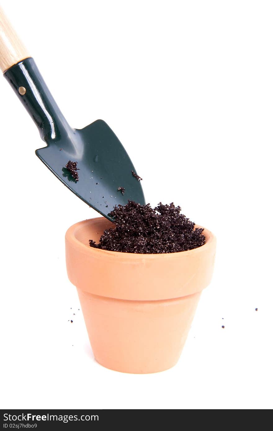 Putting soil in a terracotta pot with a garden shovel isolated over white. Putting soil in a terracotta pot with a garden shovel isolated over white