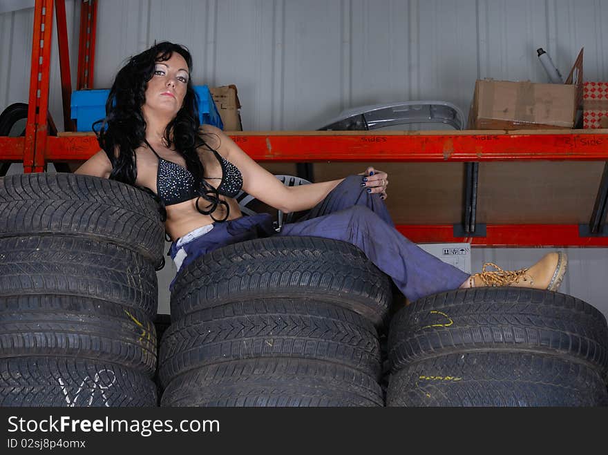 Photograph showing sexy young woman in bikini top and overalls posing on tyres. Photograph showing sexy young woman in bikini top and overalls posing on tyres