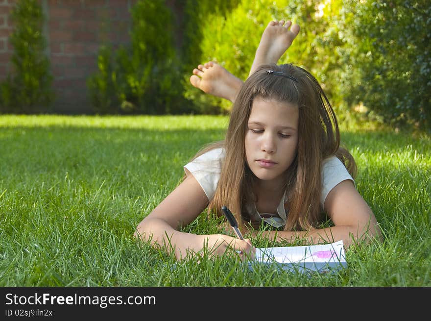 Pretty young teenage girl drawing on the paper while lying on the bed of grass.