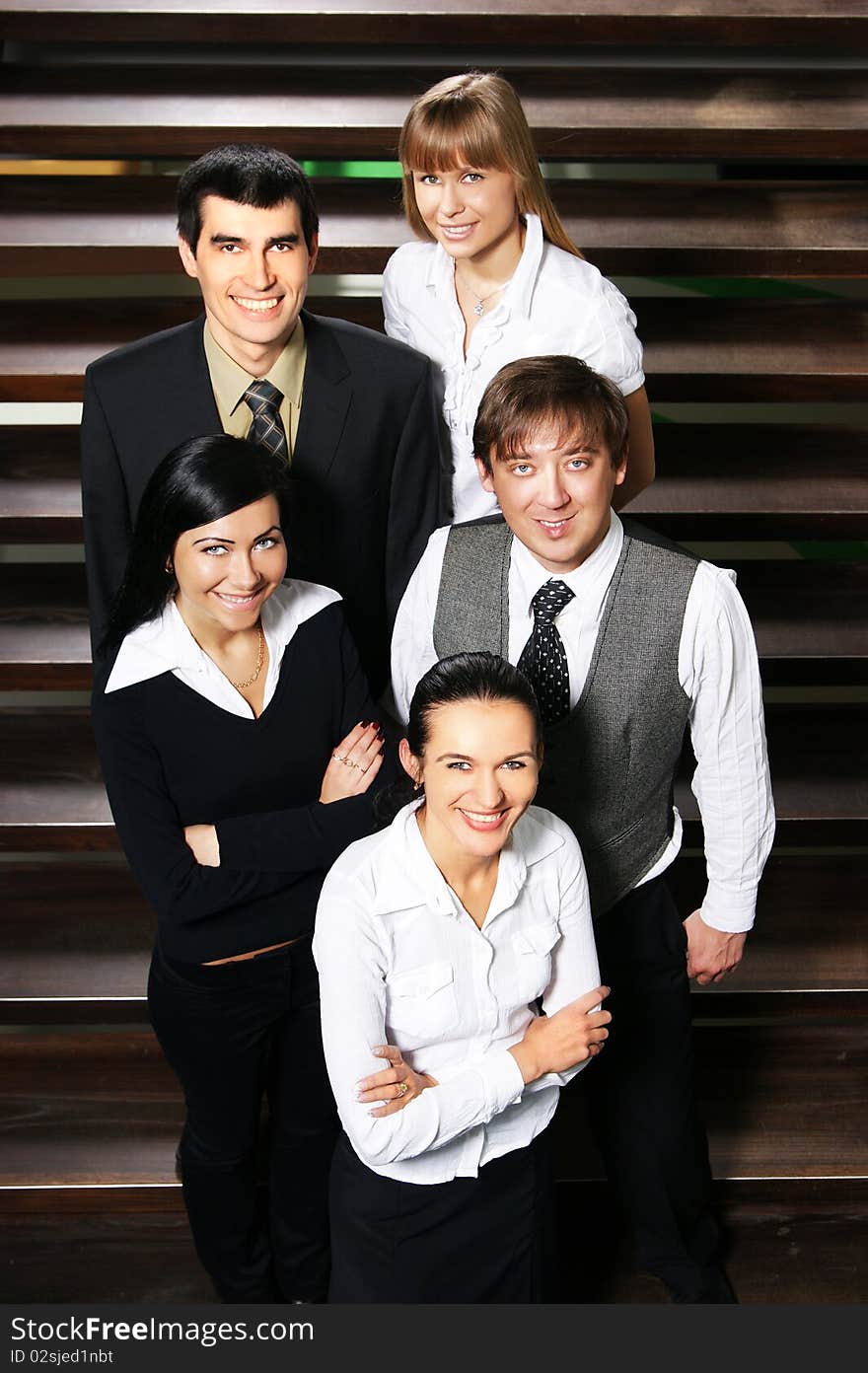 Five young business people are standing as a team with a lovely woman in front. The image is taken on the stairs.