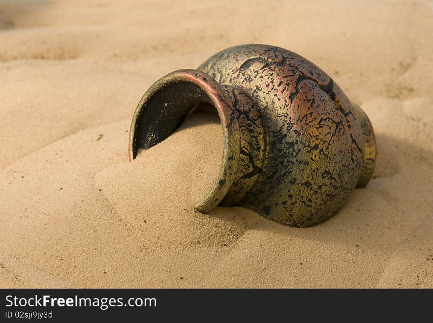 The ancient clay amphora lies on a surface of yellow sand