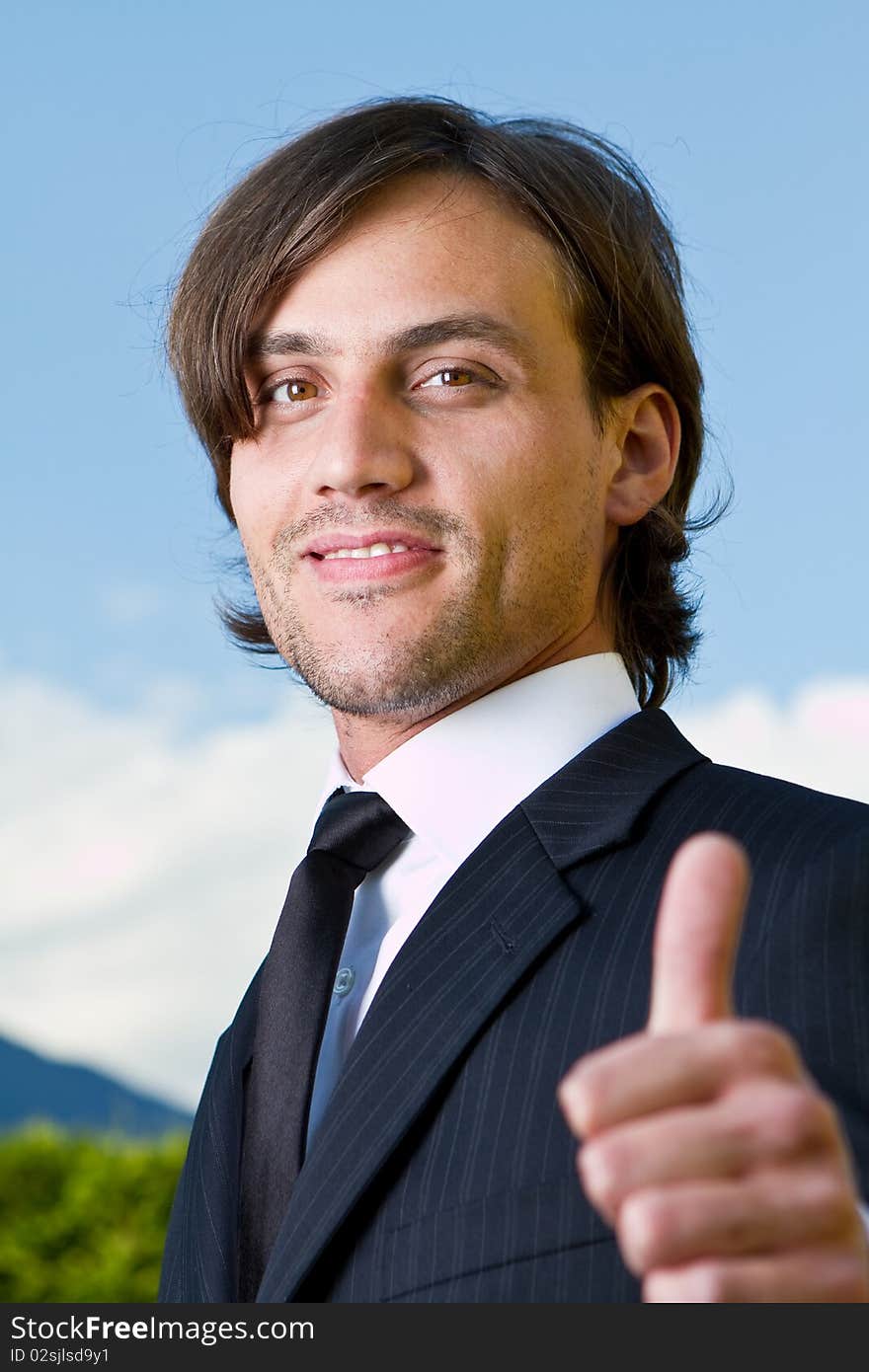 Young businessman with thumb up sign over a blue sky in the background. Young businessman with thumb up sign over a blue sky in the background.