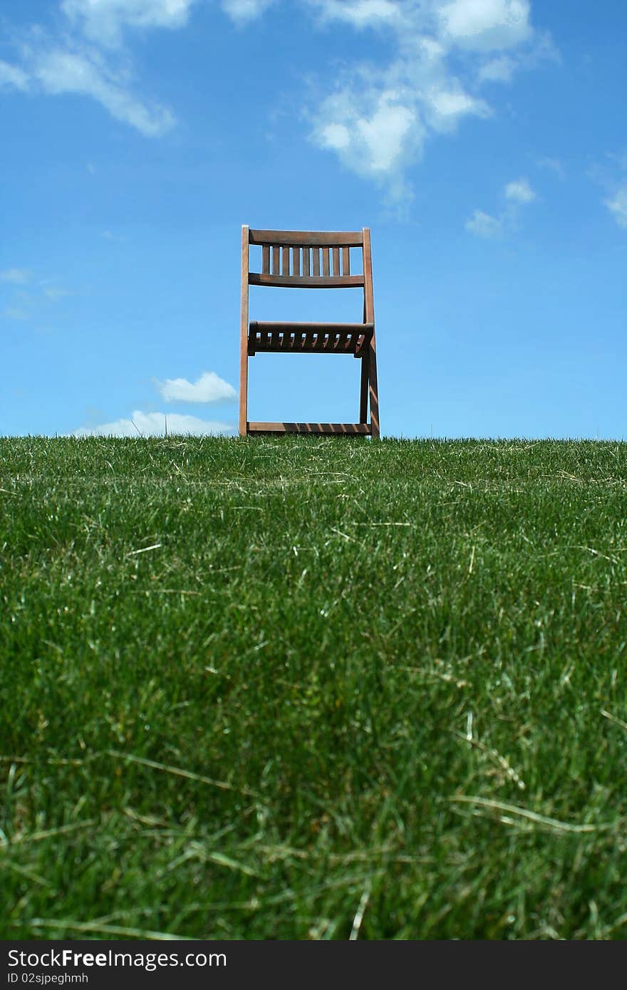 A Wooden chair with grass and sky. A Wooden chair with grass and sky