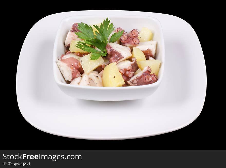 Octopus with potatoes served in a white dish. Isolated on black with clipping path