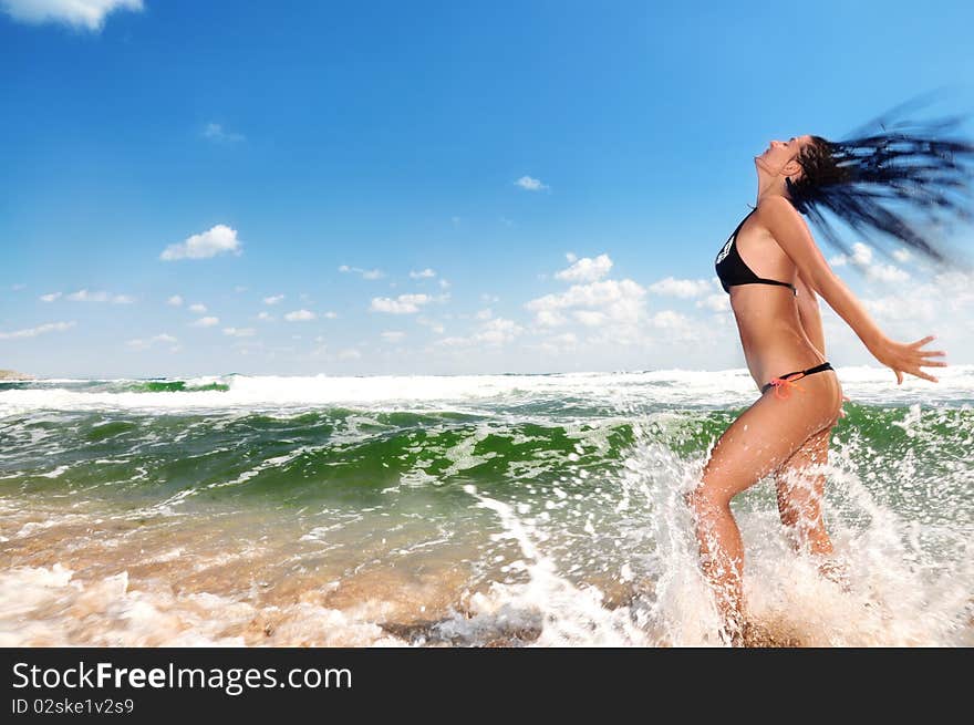 Beautiful girl splashing in the ocean, blue sky