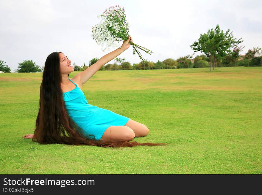 Beautiful woman with long hair sitting on the grass and enjoying nature