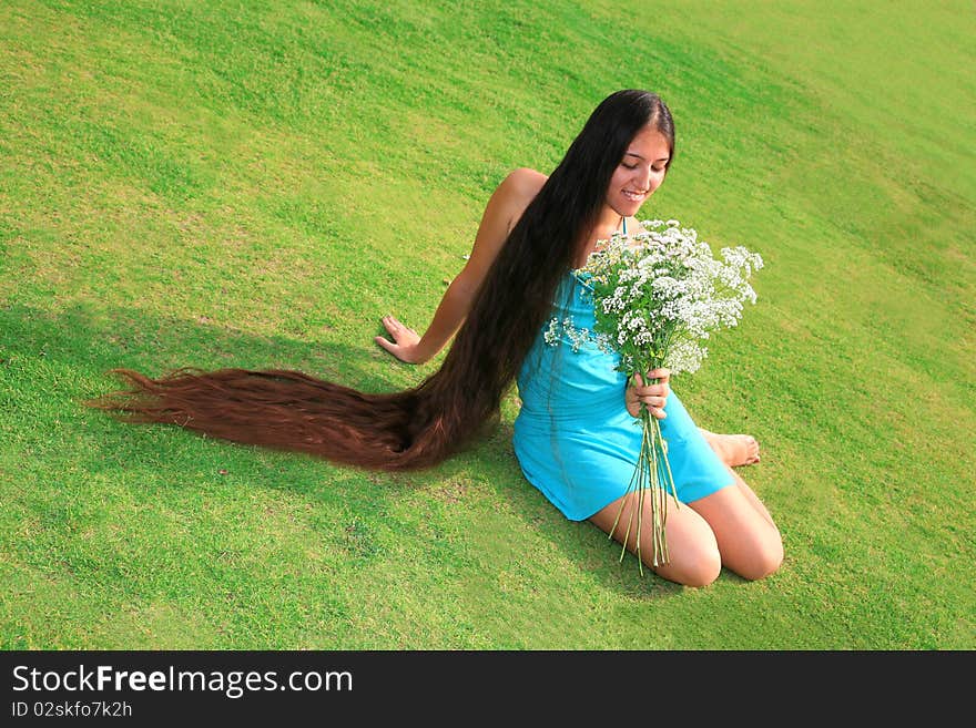 Beautiful woman with long hair sitting on the grass and enjoying nature