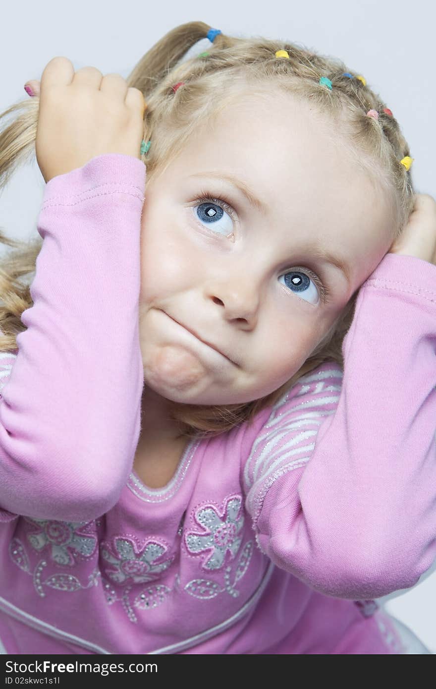 Cute young blond caucasian little girl sitting with playiful expression and looking up holding hair tails in hands isolated. Cute young blond caucasian little girl sitting with playiful expression and looking up holding hair tails in hands isolated