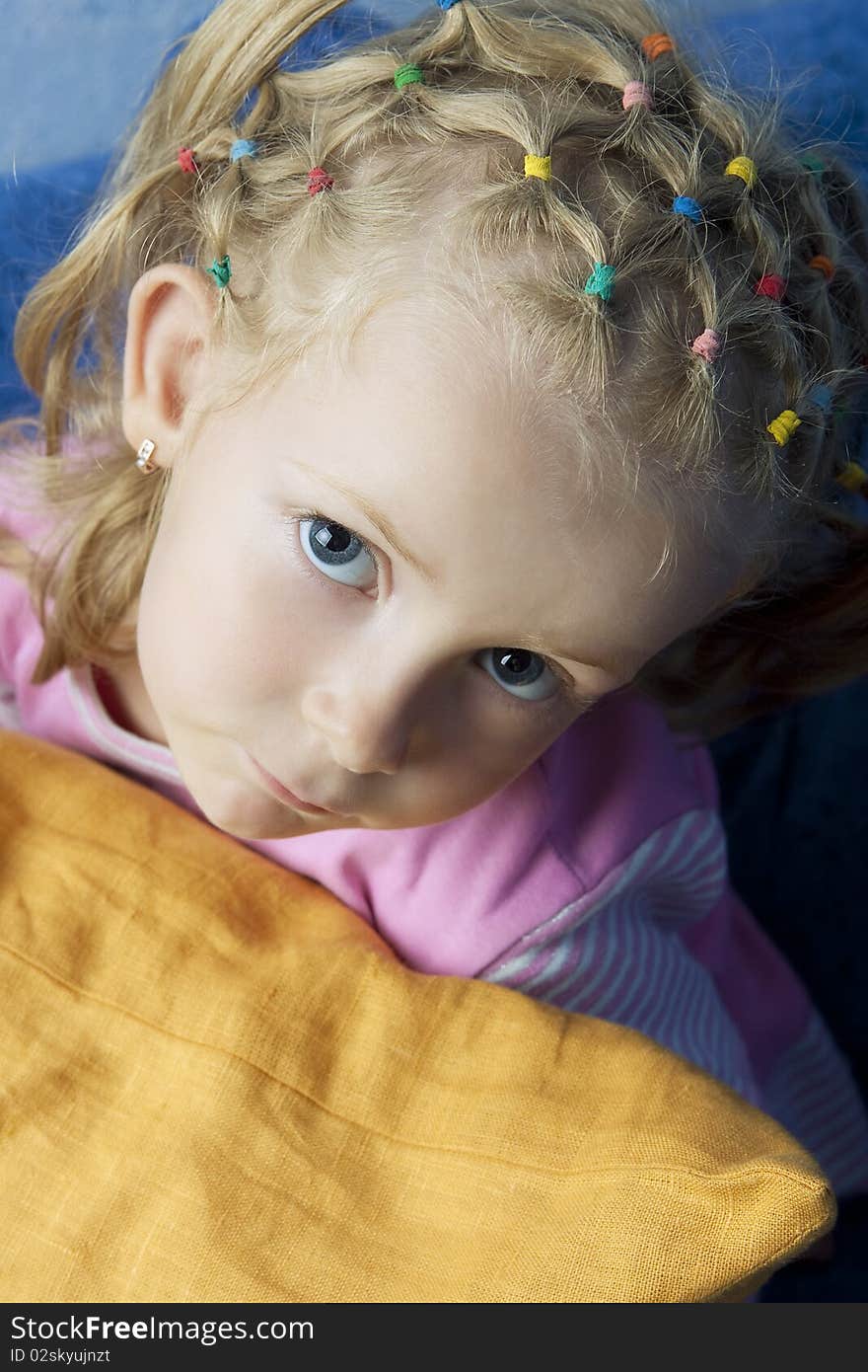 Little cute blond caucasian girl looking up with calm sincere look from behind a pillow having long hair tails on head. Little cute blond caucasian girl looking up with calm sincere look from behind a pillow having long hair tails on head