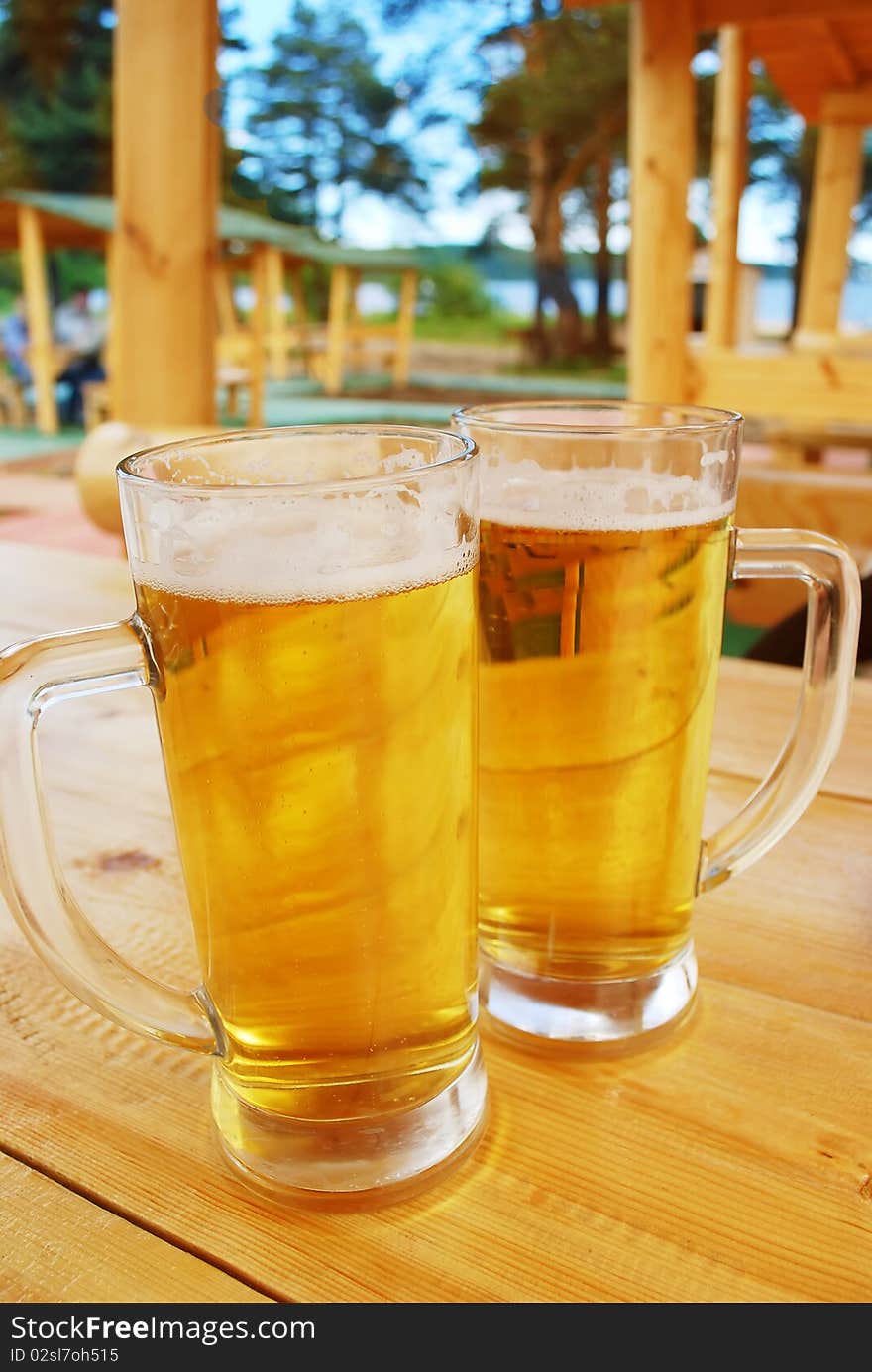 Two mugs of beer staing on the wood table in outside bar. Two mugs of beer staing on the wood table in outside bar.