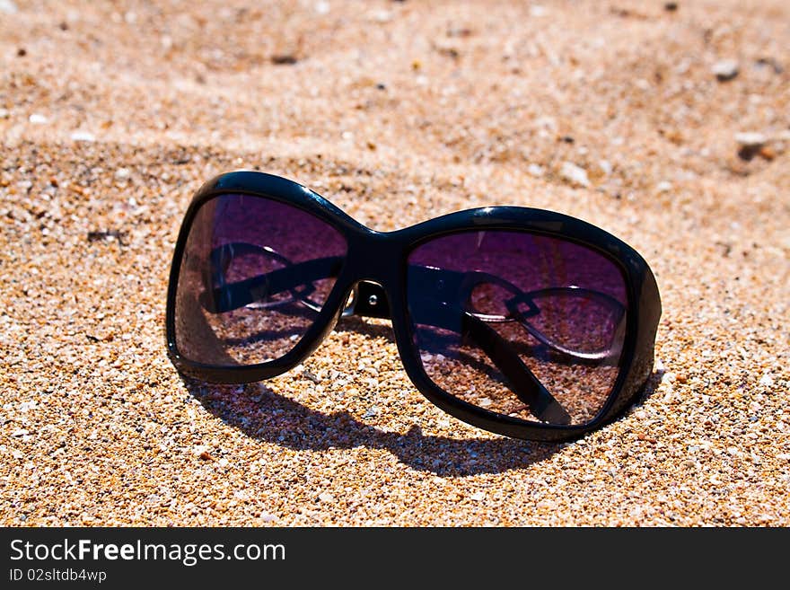 Sun glass on sand background